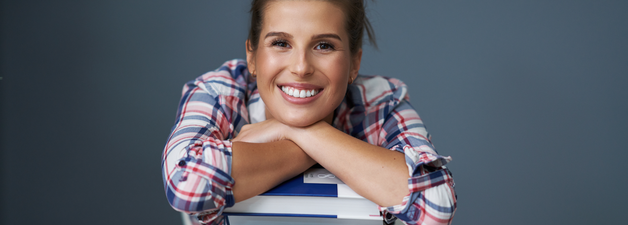 Jonge meid met haar armen op een stapel boeken achter haar bureau