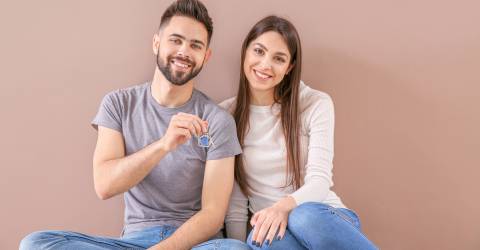 Jon stel met huissleutels van hun nieuwe huis in hun hand zitten voor een gekleurde muur